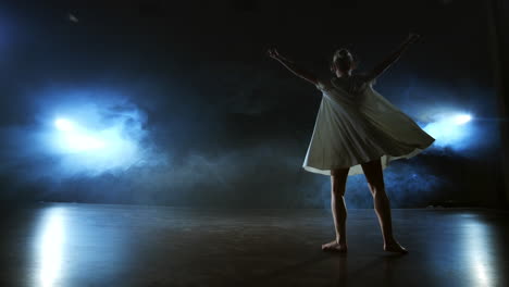 Modern-dance-girl-in-a-white-dress-dances-a-modern-ballet-jumps-on-the-stage-with-smoke-in-the-blue-spotlights.
